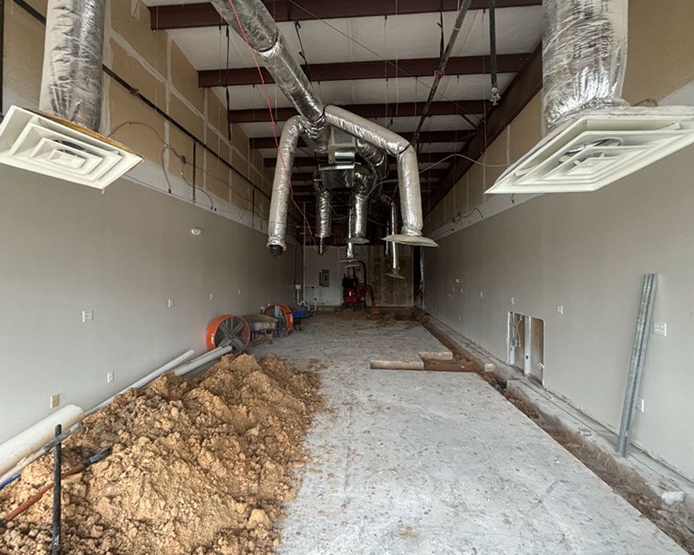 Interior view of a commercial construction site with exposed ductwork, piles of dirt, and construction equipment, illustrating ground-up construction services by Kinetic Builders Corp.