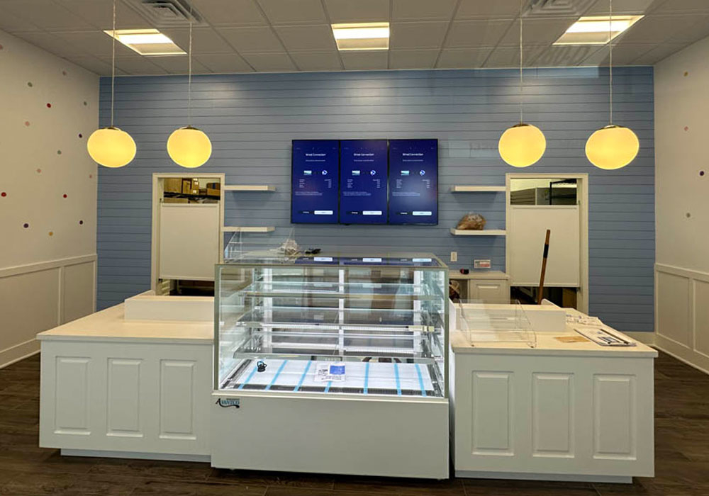 Modern restaurant interior featuring a sleek service counter with a glass display case, digital screens showing HVAC system data, and stylish pendant lighting, emphasizing advanced climate control and energy efficiency innovations.