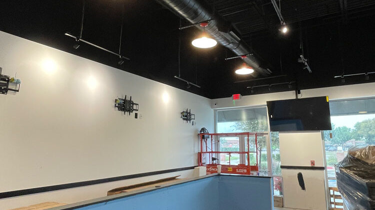 Interior view of a commercial construction site featuring wall-mounted brackets, lighting fixtures, and a scaffold, indicative of ongoing build-out and installation processes for Kinetic Builders Corp.'s services.