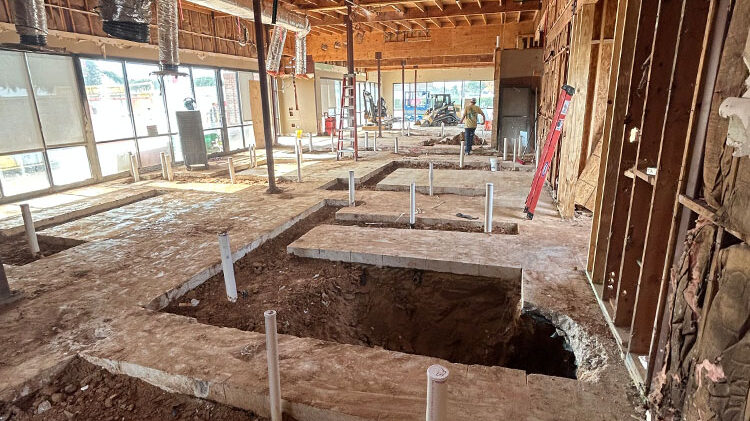 Interior construction site with exposed flooring, plumbing pipes, and a worker preparing for ground-up commercial build, showcasing Kinetic Builders' pre-construction services.