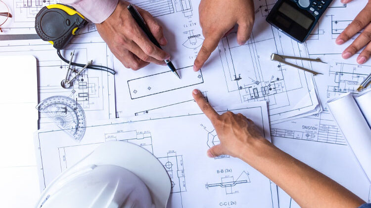 Hands reviewing construction blueprints and plans with tools, emphasizing project management in commercial construction.