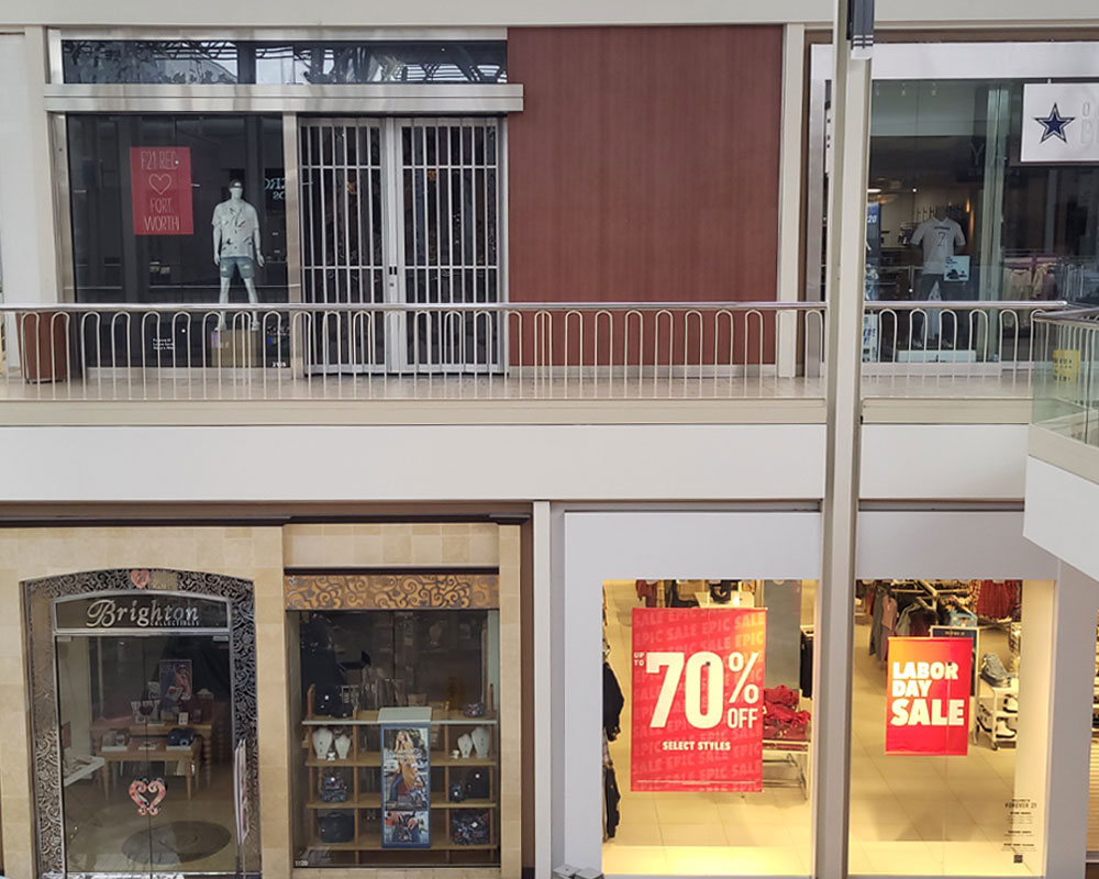 Retail storefronts in a mall featuring promotional signage, including "Labor Day Sale" and "Up to 70% Off Select Styles," showcasing vibrant displays for tenant build-outs and retail improvements by Kinetic Builders Corp.
