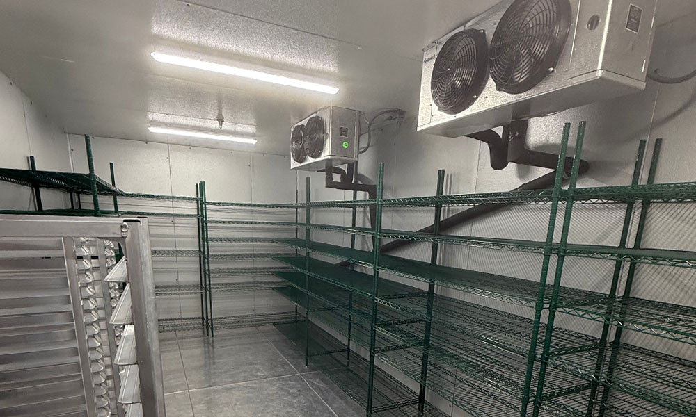Commercial bakery storage area with metal shelving, industrial refrigeration units, and bright overhead lighting, designed for high-volume food retail operations like Nothing Bundt Cakes.