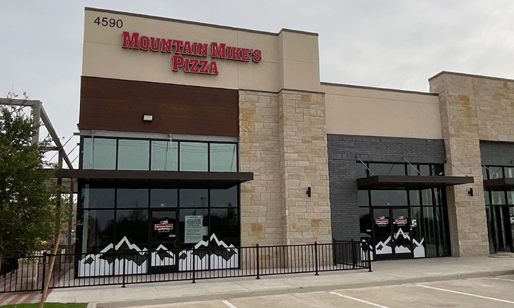 Mountain Mike's Pizza restaurant exterior with signage, featuring a modern design and large glass windows, located in Texas, showcasing brand identity and welcoming atmosphere.