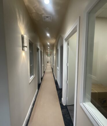 Commercial construction hallway with illuminated walls, finished flooring, and doorways leading to offices, showcasing Kinetic Builders Corp's craftsmanship in a completed project.