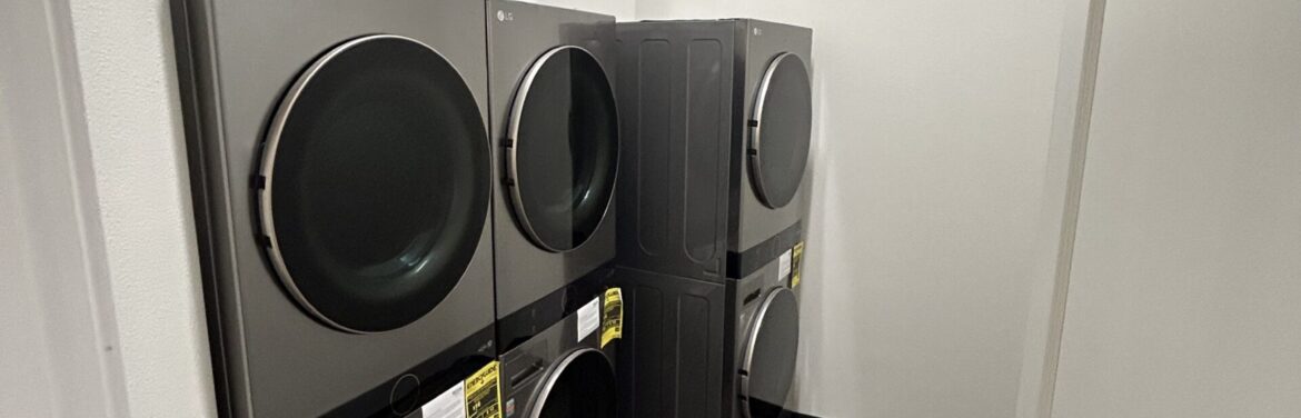 Commercial laundry appliances installed in a modern facility, featuring stacked LG washer and dryer units against a neutral wall, showcasing Kinetic Builders Corp.'s expertise in commercial construction and interior design.