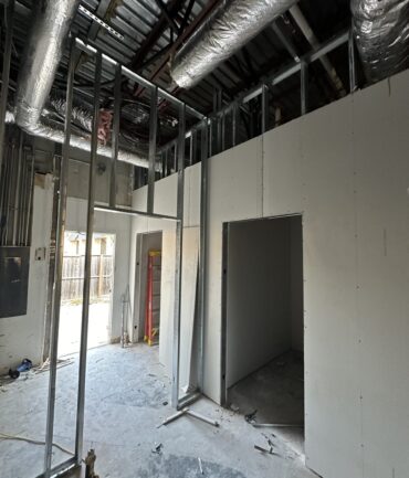 Interior construction site with metal framing, drywall, and exposed ductwork, showcasing progress on commercial build-out by Kinetic Builders Corp.