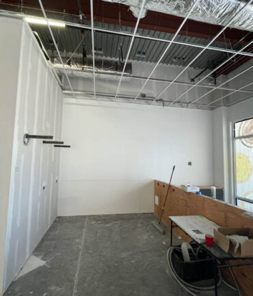 Interior of a commercial construction project featuring unfinished drywall, exposed ceiling, and a wooden counter, illustrating Kinetic Builders Corp.'s commitment to quality and precision in restaurant build-outs.
