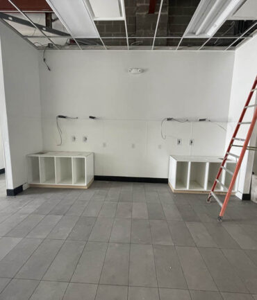 Commercial construction site interior with unfinished walls, two base cabinets, exposed electrical wiring, and a ladder, showcasing Kinetic Builders Corp.'s work in progress for a restaurant build-out.