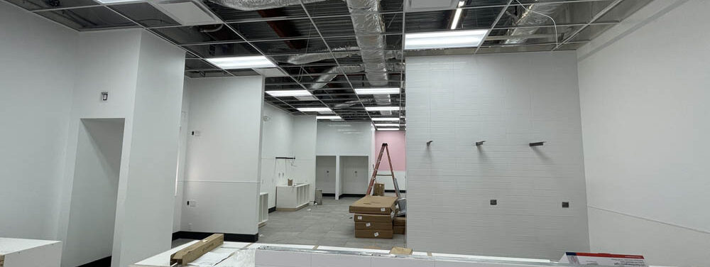 Commercial construction interior showcasing a partially finished space with white walls, ceiling fixtures, and construction materials, reflecting Kinetic Builders Corp's commitment to quality and precision in restaurant build-outs.