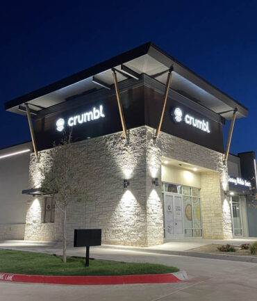 Crumbl Cookies storefront illuminated at night, showcasing modern architecture and branding, part of Kinetic Builders Corp's commercial construction portfolio.