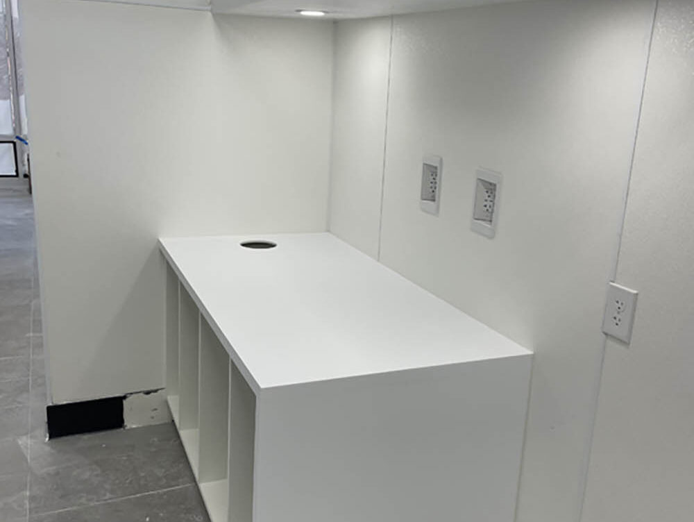 White commercial countertop with electrical outlets and a circular cutout, showcasing Kinetic Builders Corp.'s craftsmanship in interior construction.