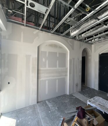 Interior view of a commercial construction space featuring drywall installation, arched openings, and exposed ceiling framework, showcasing Kinetic Builders Corp.'s craftsmanship in project development.