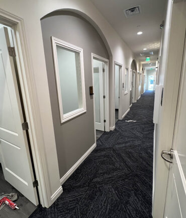 Commercial construction hallway with arched entryways, framed windows, and carpeted flooring, showcasing Kinetic Builders Corp.'s interior design craftsmanship.