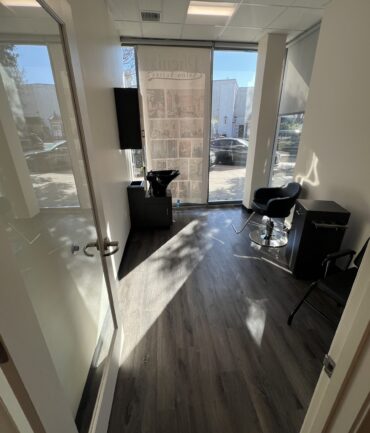 Interior view of a modern commercial space featuring sleek flooring, a black chair, a small table, and large windows allowing natural light, reflecting Kinetic Builders Corp.'s commitment to quality in commercial construction projects.