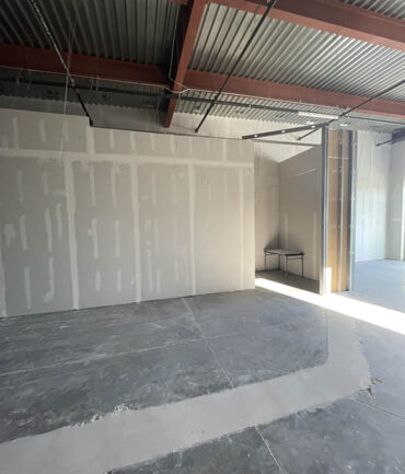Commercial construction interior showcasing drywall installation and unfinished flooring in a large, open space.