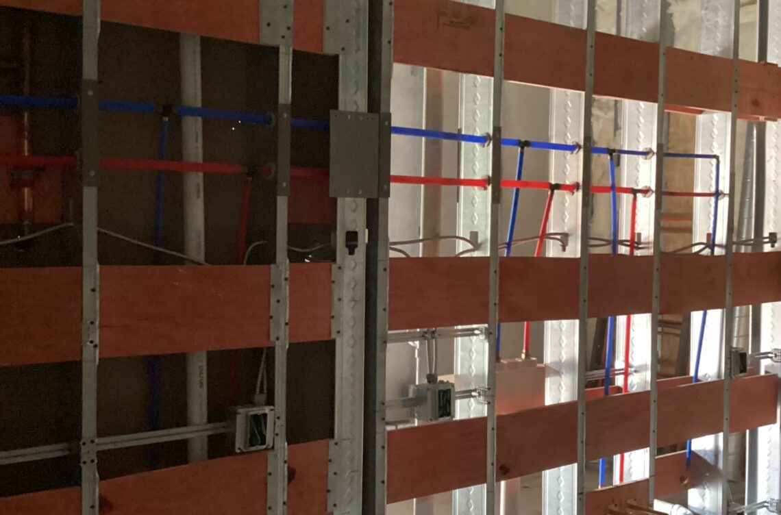 Interior construction framework featuring red and blue piping, electrical boxes, and wooden panels, illustrating Kinetic Builders Corp's commercial construction work.
