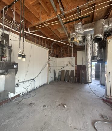 Commercial kitchen construction site with exposed wiring, ductwork, and unfinished walls, showcasing Kinetic Builders Corp's focus on high-impact restaurant build-outs.