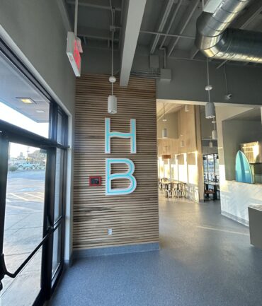 Interior view of a commercial space featuring a wood-paneled wall with illuminated "HB" signage, showcasing Kinetic Builders Corp.'s craftsmanship in restaurant build-out projects.