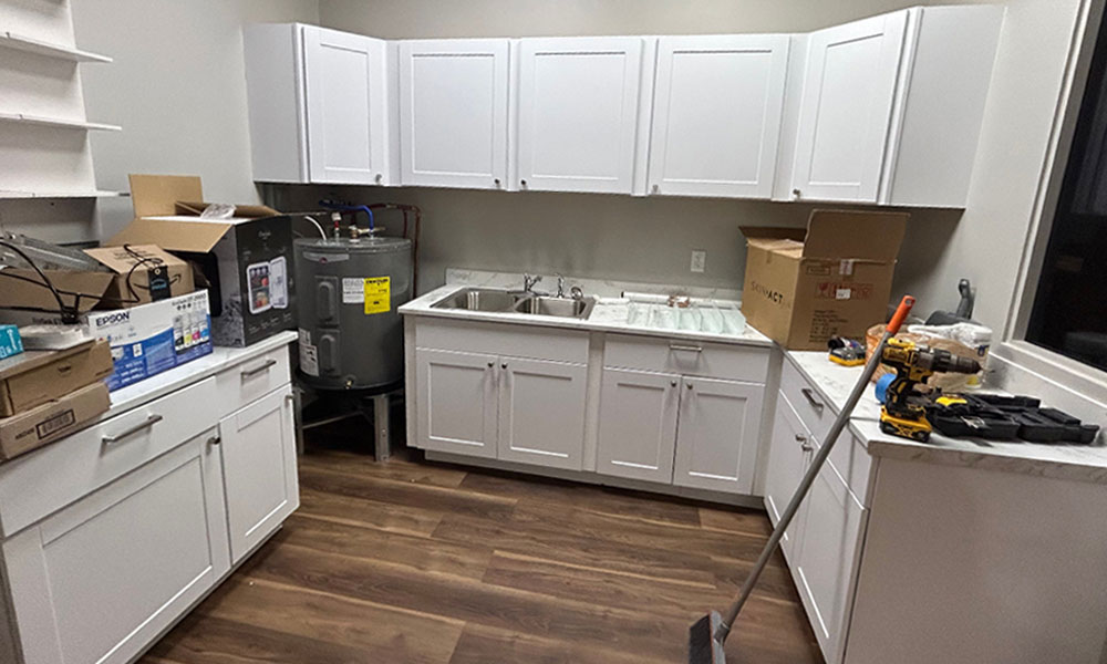 Kitchen space under construction for Prime IV Hydration & Wellness, featuring white cabinetry, a sink, and various construction materials, illustrating the tenant build-out process.