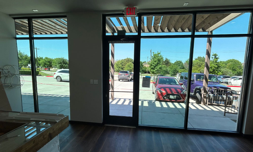 Interior view of Prime IV Hydration & Wellness entrance, showcasing large glass doors and windows with natural light, wooden ceiling beams, and a welcoming atmosphere, highlighting the retail wellness space designed for client comfort and functionality.