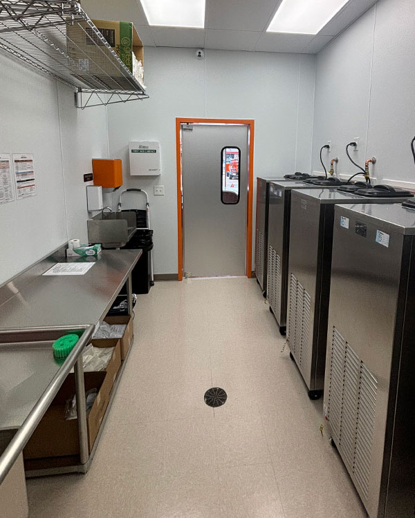 Commercial kitchen space featuring stainless steel counters, industrial refrigerators, and an orange-accented door, emphasizing Kinetic Builders Corp's focus on quality construction in restaurant facilities.