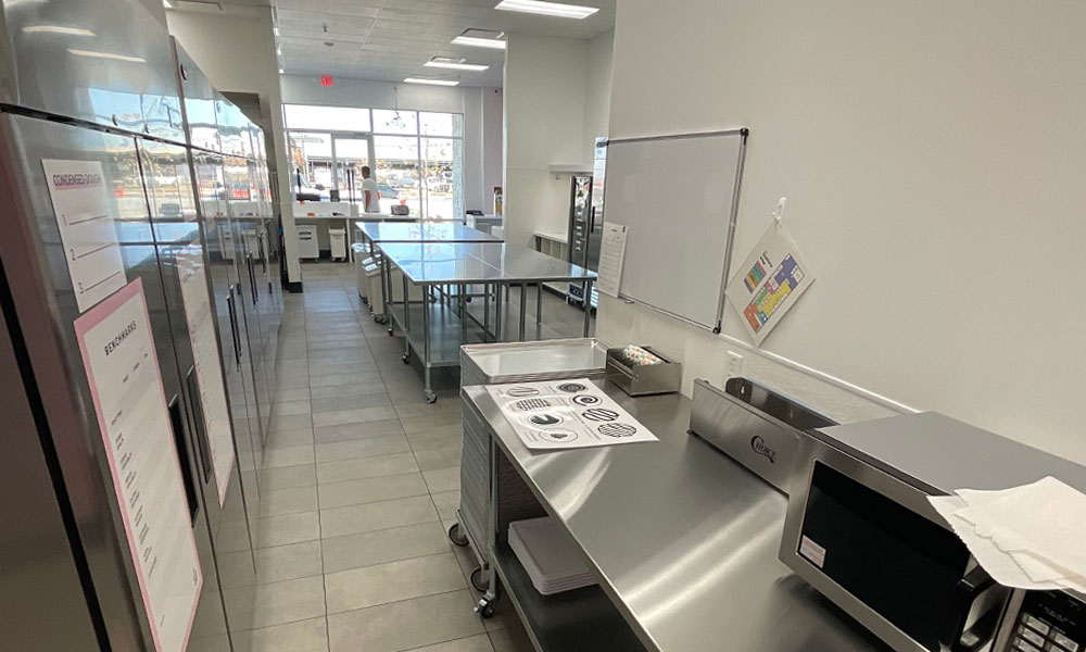 Modern commercial kitchen interior for Crumbl Cookies, featuring stainless steel workstations, organized storage, and operational equipment, emphasizing high-performance design for efficient baking and food service.