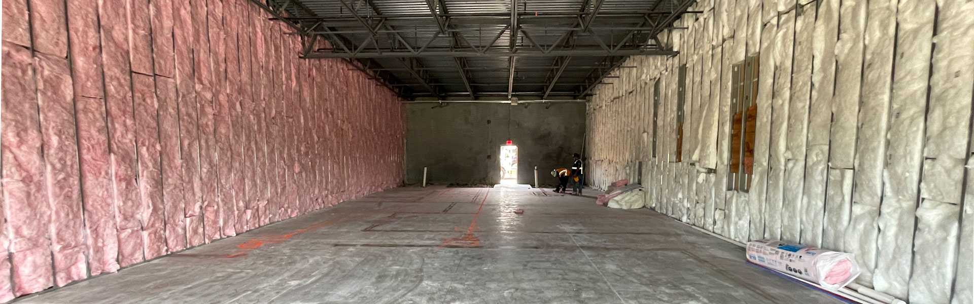 Construction site interior with insulated walls, workers in safety gear, and unfinished flooring, showcasing Kinetic Builders Corp's commitment to tailored commercial spaces for various industries.