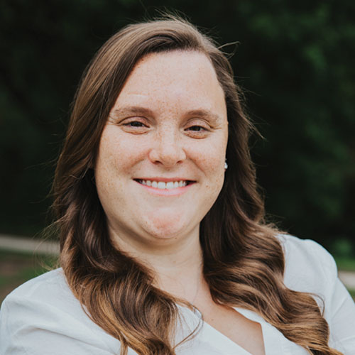 Katelyn Ellis, Comptroller and Office Manager at Kinetic Builders Corp, smiling outdoors with wavy hair and a white blouse, representing the company's commitment to leadership and professional expertise in commercial construction.