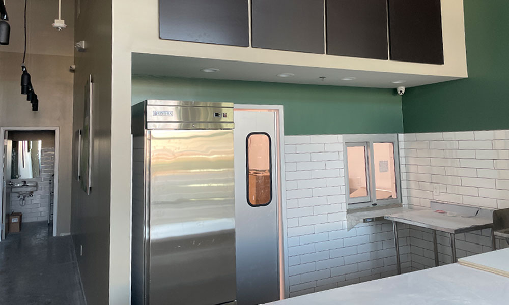 Interior view of a Nekter Juice Bar location featuring a stainless steel refrigerator, white tiled walls, and modern design elements, showcasing the franchise's focus on clean, functional spaces for food retail.