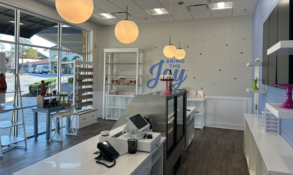 Bright bakery interior of Nothing Bundt Cakes featuring a welcoming order counter, colorful decor, and display shelves, emphasizing brand identity and inviting atmosphere.