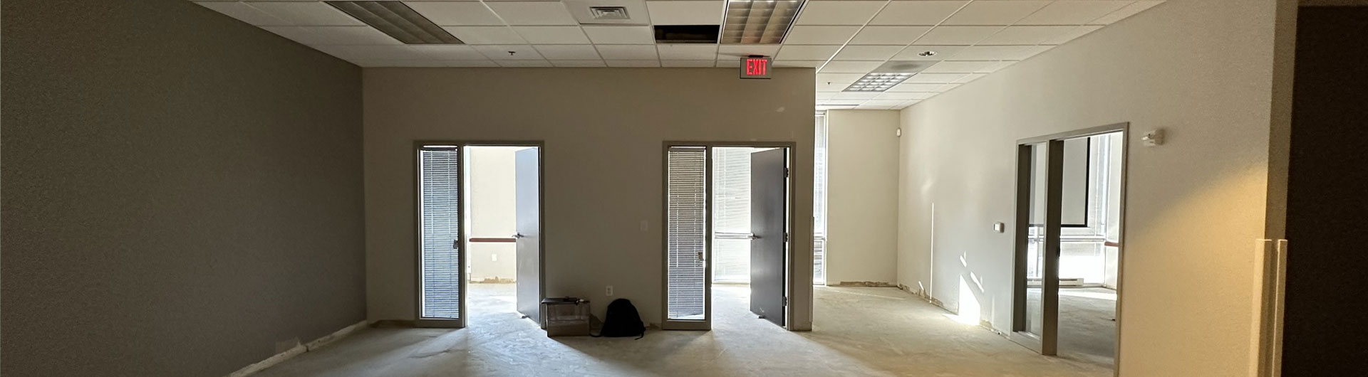 Empty commercial space with multiple doors, unfinished flooring, and neutral wall colors, representing Kinetic Builders' expertise in retail and tenant build-outs.