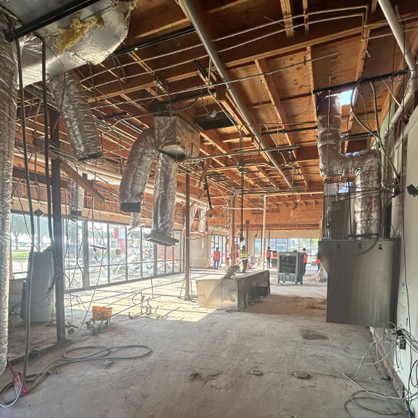 Construction site interior showing exposed ductwork, unfinished ceiling, and equipment, highlighting Kinetic Builders Corp.'s commercial project progress.