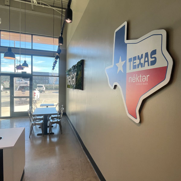 Texas map sign featuring the Nékter Juice Bar logo in a modern commercial space with seating area and large windows.