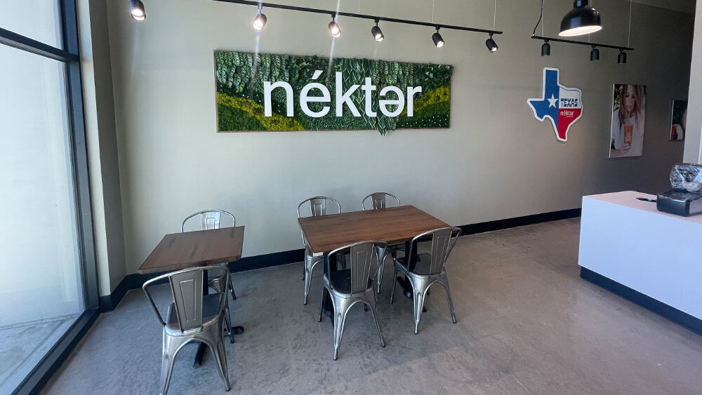 Interior of a restaurant featuring modern design elements, including metal chairs and wooden tables, with a prominent green and white "néktər" sign on the wall, symbolizing a welcoming atmosphere for guests in compliance with restaurant build-out standards.