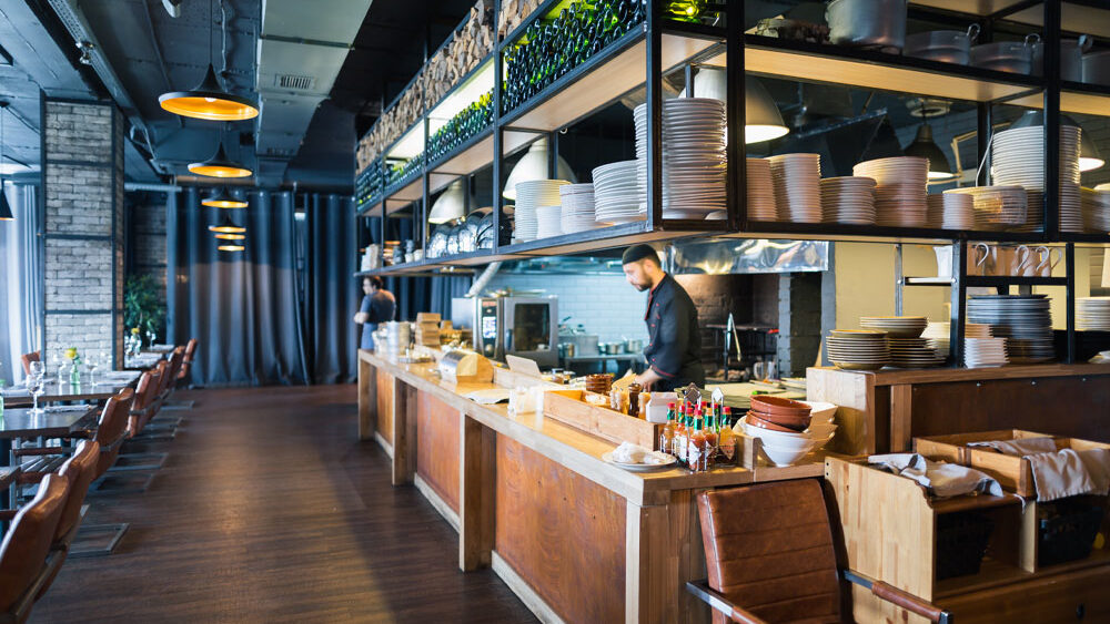 Restaurant interior featuring a modern design with wooden counters, stacked plates, and a chef preparing food, illustrating Kinetic Builders' expertise in restaurant tenant improvements.