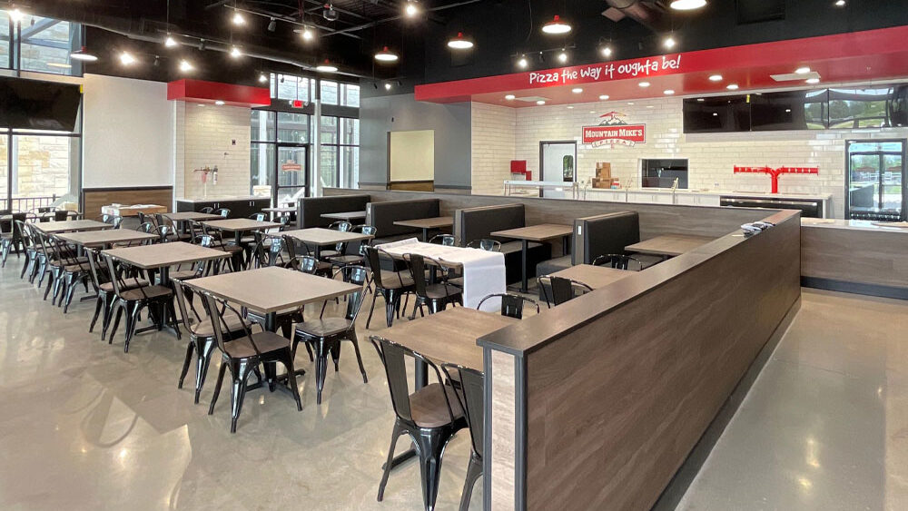 Restaurant interior featuring tables and chairs, modern design with a service counter displaying "Mountain Mike's" branding, emphasizing restaurant tenant improvements and dining space layout.