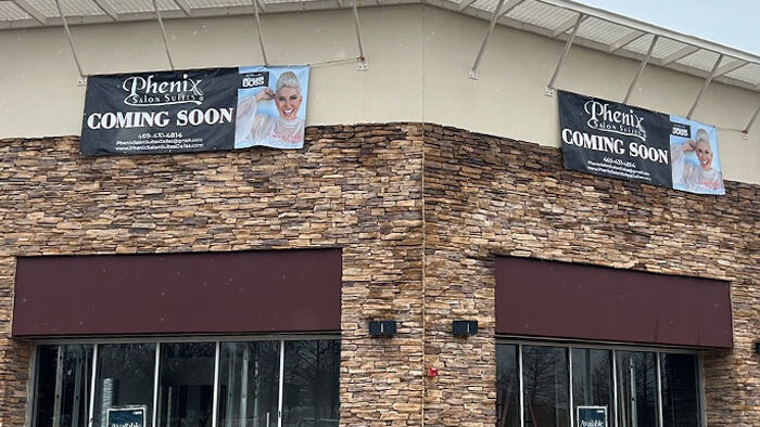 Phenix Salon Suites storefront with "COMING SOON" banners, featuring a stone facade and large windows, indicating future tenant improvements for a salon space.