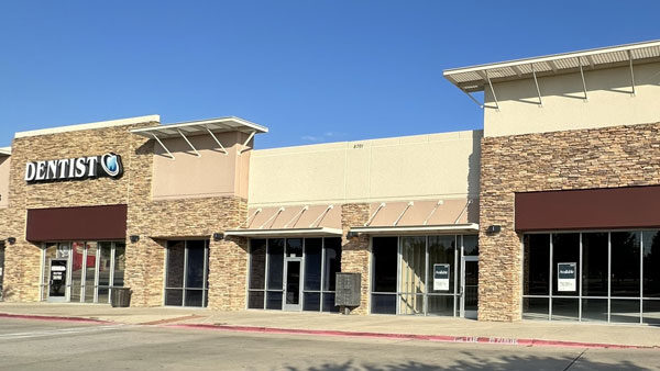 Dentist office exterior in a retail plaza, featuring stone facade and large windows, with vacant storefronts nearby.
